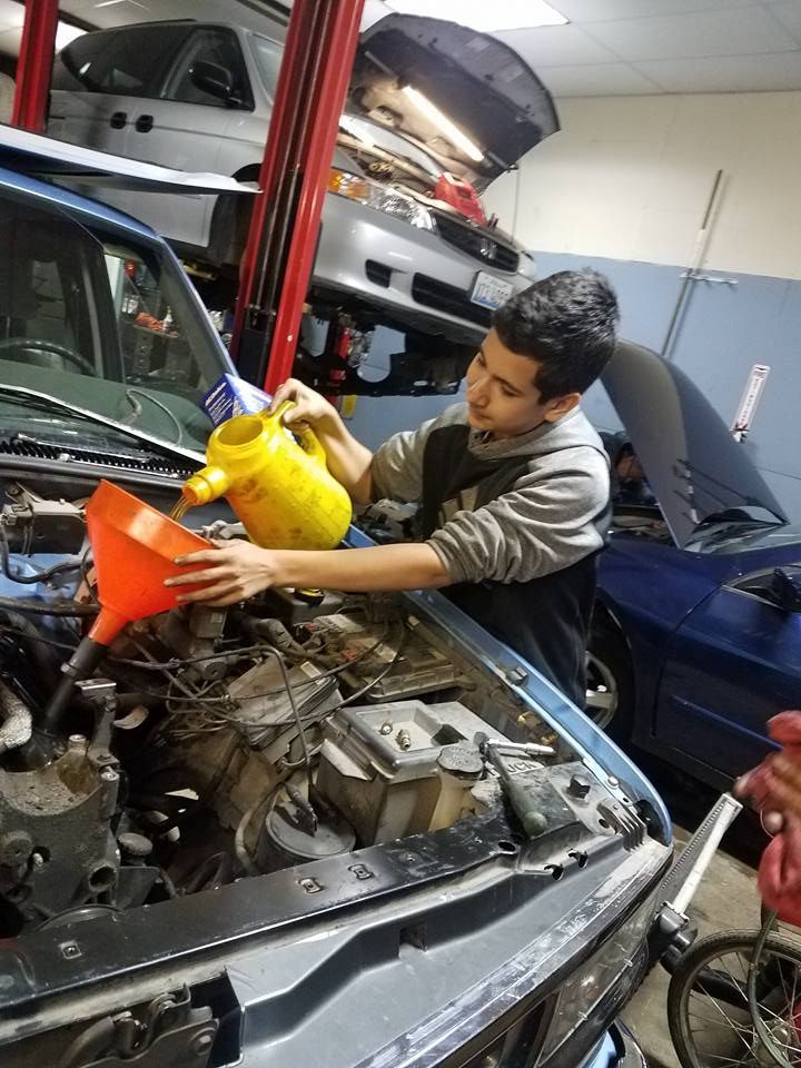Person pouring liquid from a yellow container into a car engine with a funnel in a garage.