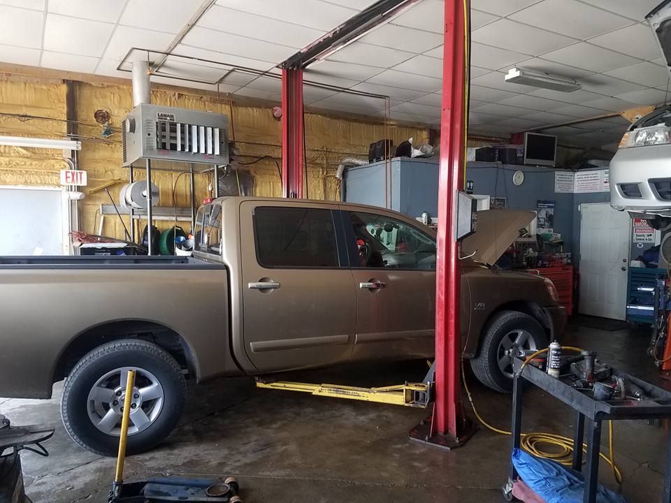 Tan pickup truck on a lift in a repair shop, hood open.