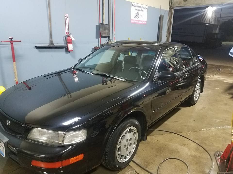 Black Nissan Maxima sedan parked inside a garage. The car is shiny, and has silver wheels.
