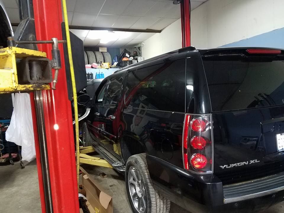 Black SUV on a lift in a garage. Red lift columns, open bay, and tools are visible.