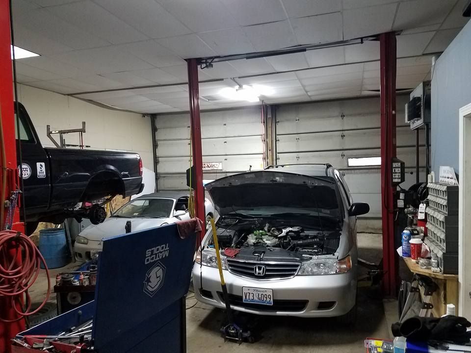 An auto repair shop with a car on a lift and another with its hood open. A truck is also present.