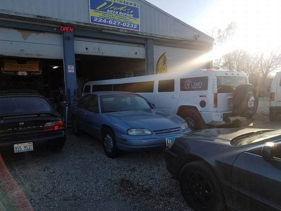 Cars parked in front of an auto repair shop with a white limousine and an open garage door.