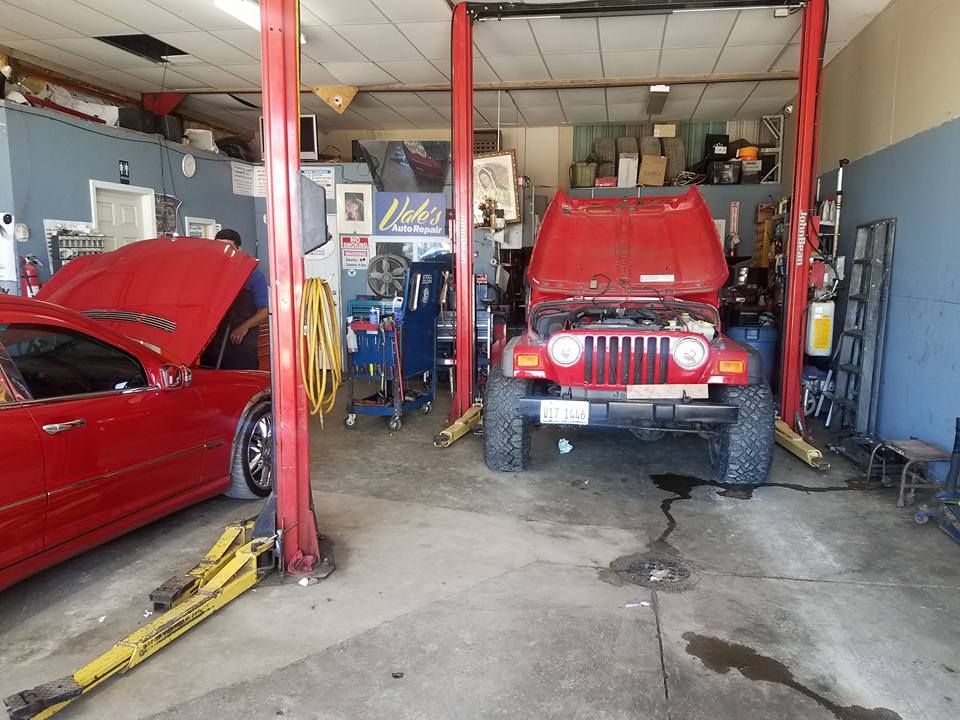 Interior of a car repair shop with two red cars, one on a lift, and tools visible.