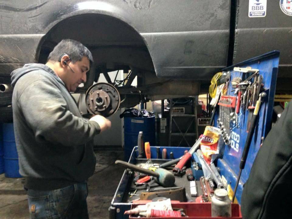 Mechanic working on car's brakes at a repair shop, tools visible. He is focused, wearing a gray hoodie.