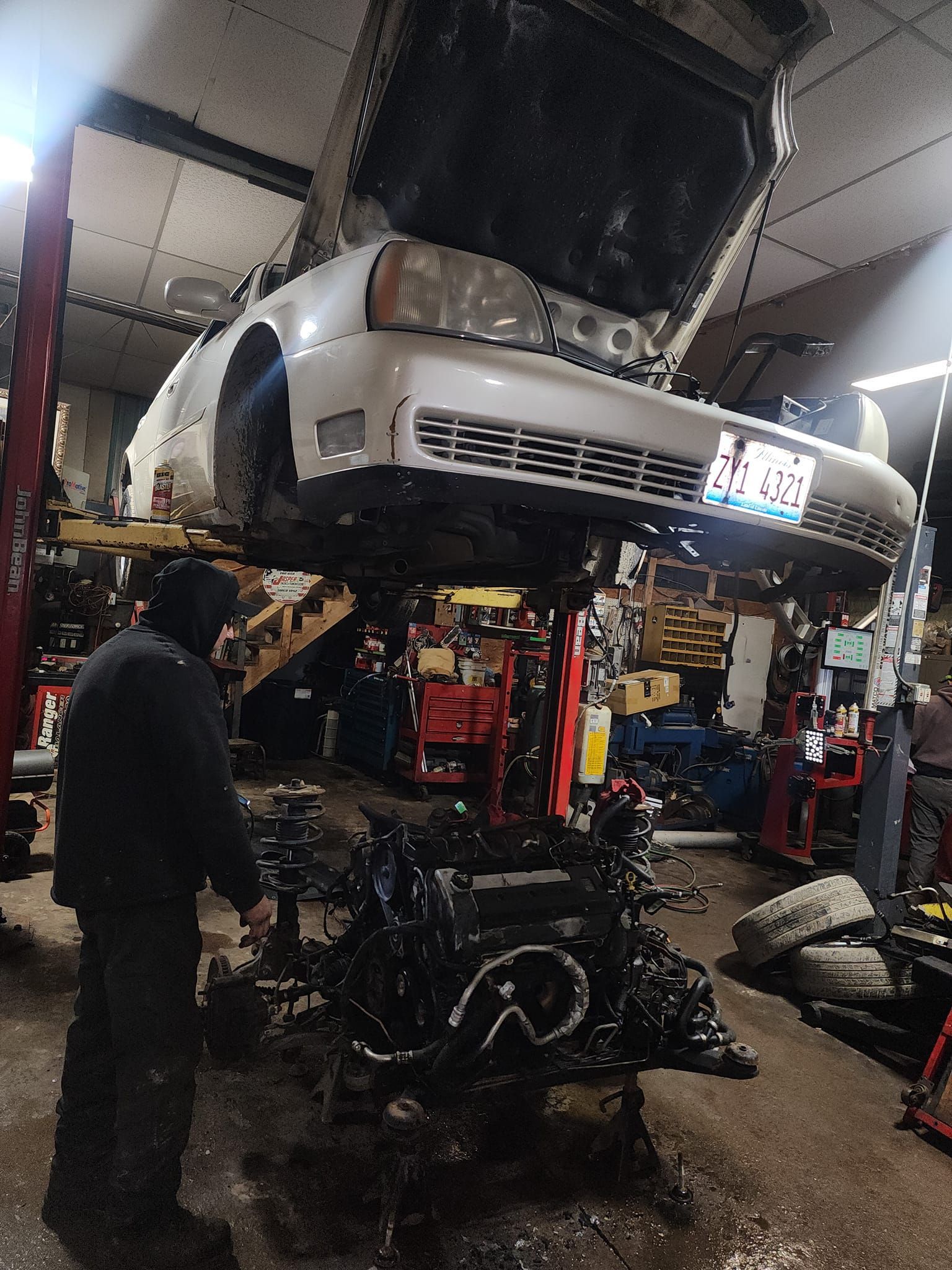 Car being repaired in a shop. Engine removed from vehicle raised on a lift. Mechanic looking at engine.