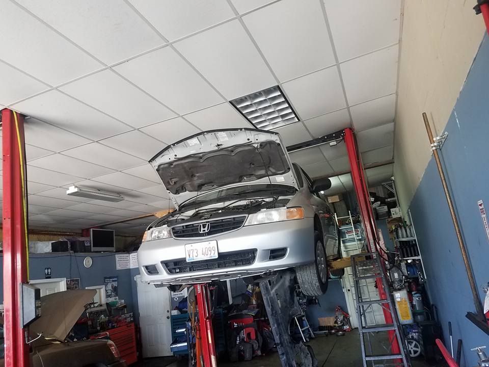 Silver car raised on a lift in a repair shop, hood open, ready for service.