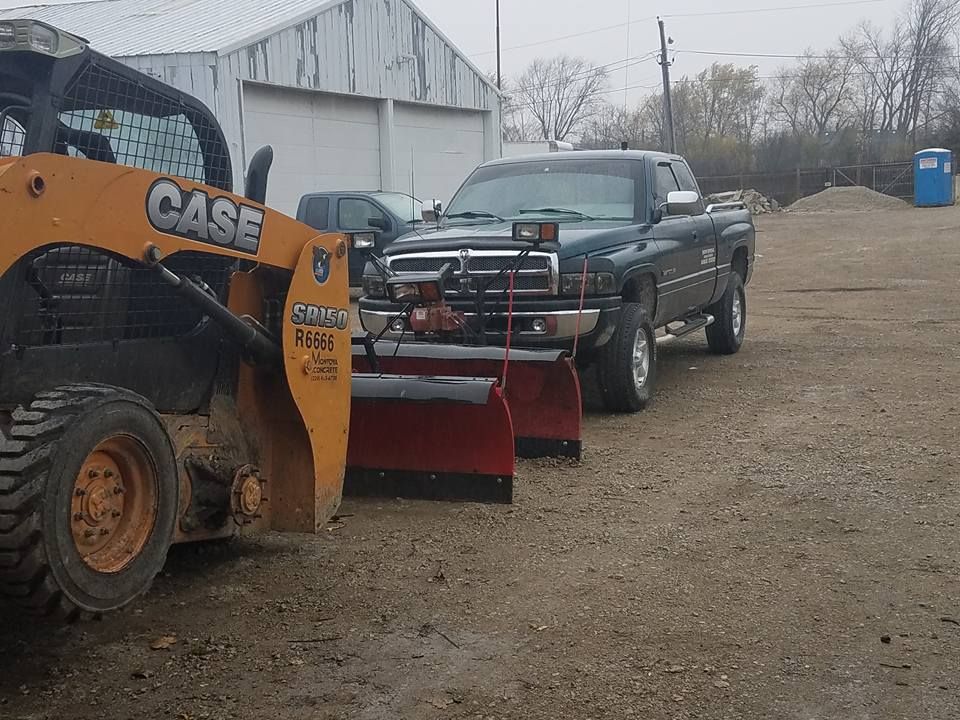 A green pickup truck with a snowplow is next to a CASE skid steer loader on a gravel lot.