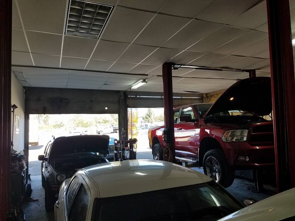 Cars inside a repair shop with open hoods. One red truck lifted on a hoist near an open garage door.