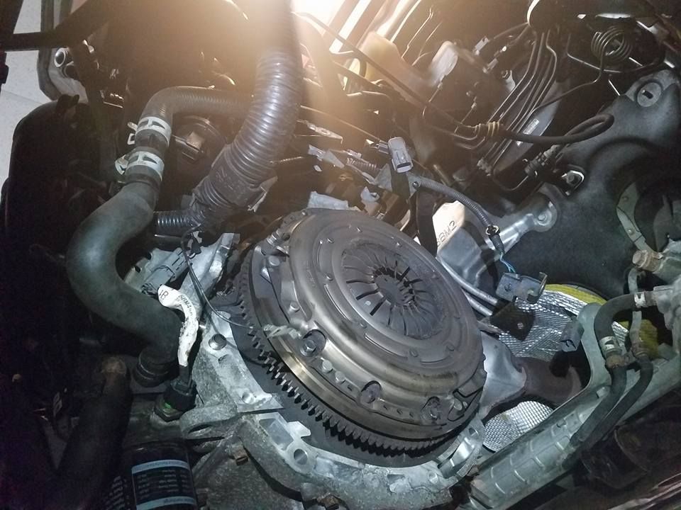 Engine compartment with clutch assembly visible; various hoses and components are also present.