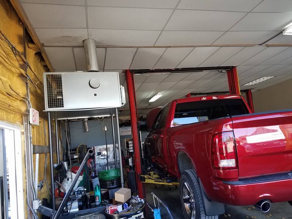 Red pickup truck on a lift inside a garage, with equipment and a heating unit visible.
