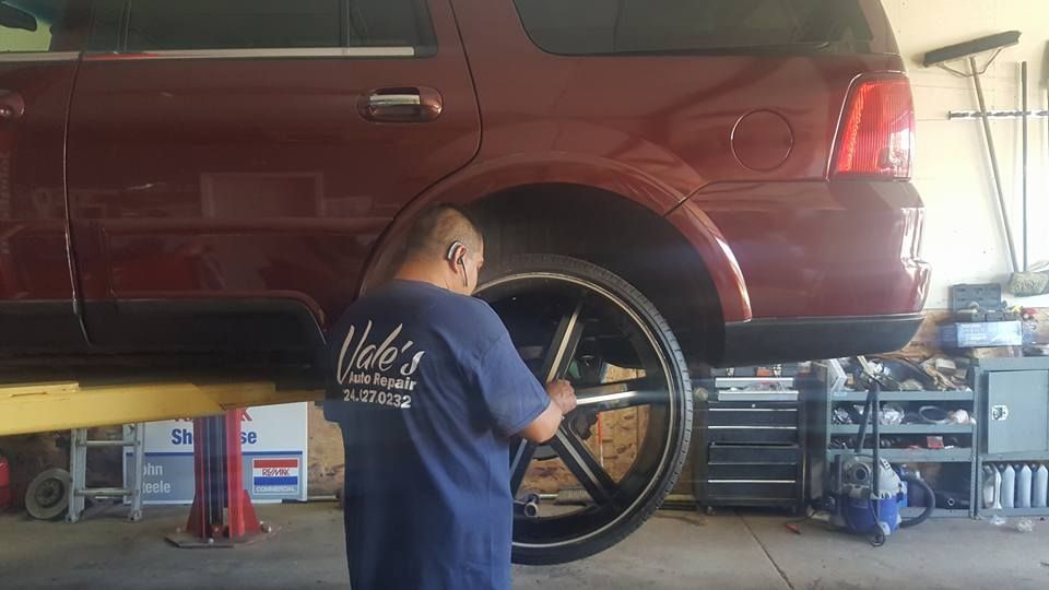 Mechanic working on a lifted maroon SUV's large wheel in a garage.