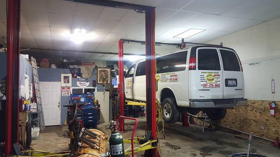 Van lifted on a red car lift inside a cluttered repair shop; tools and equipment surround the vehicle.