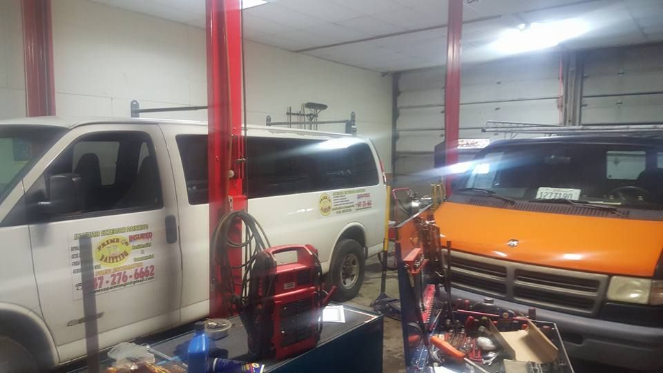 Two vans in a garage; a white one and an orange one. Red car lift, tools and equipment visible.