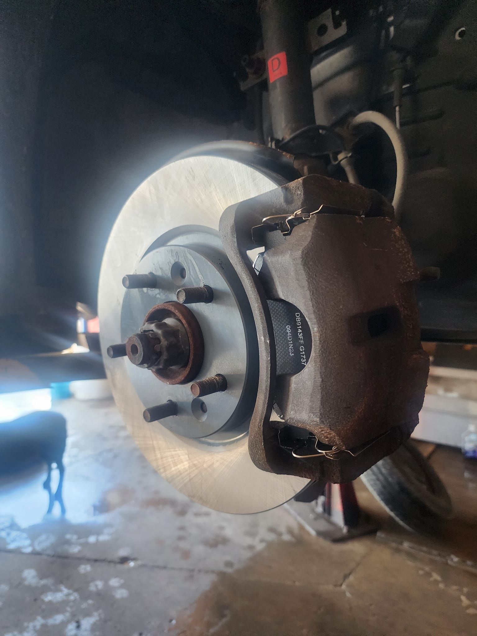 Car brake disc and caliper, wheel removed, on a jack.