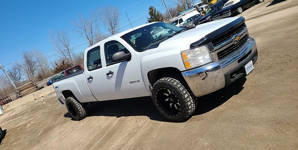 Silver pickup truck with black wheels on dirt under a blue sky.