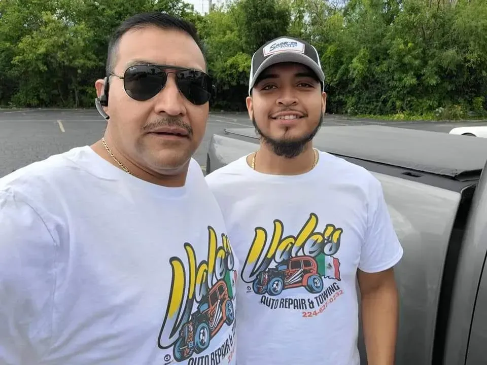 Two men in matching white shirts pose outside, likely at a food truck. They are smiling.