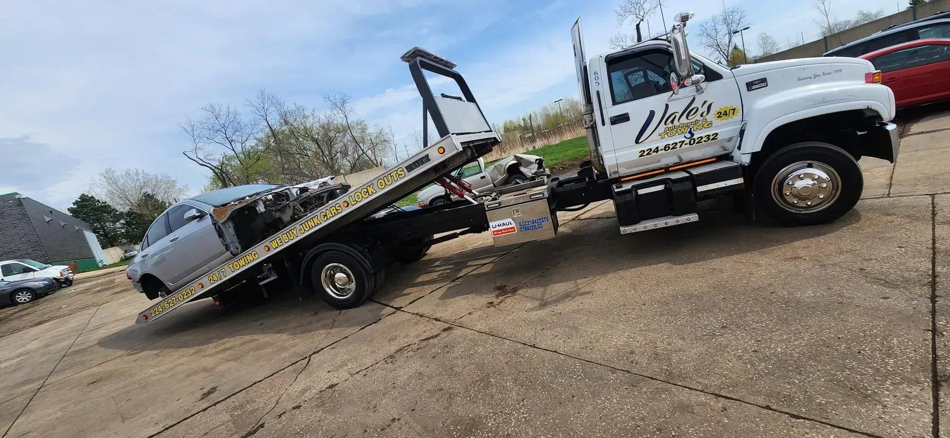 Tow truck carrying a silver car up a ramp on a paved surface. White tow truck with 