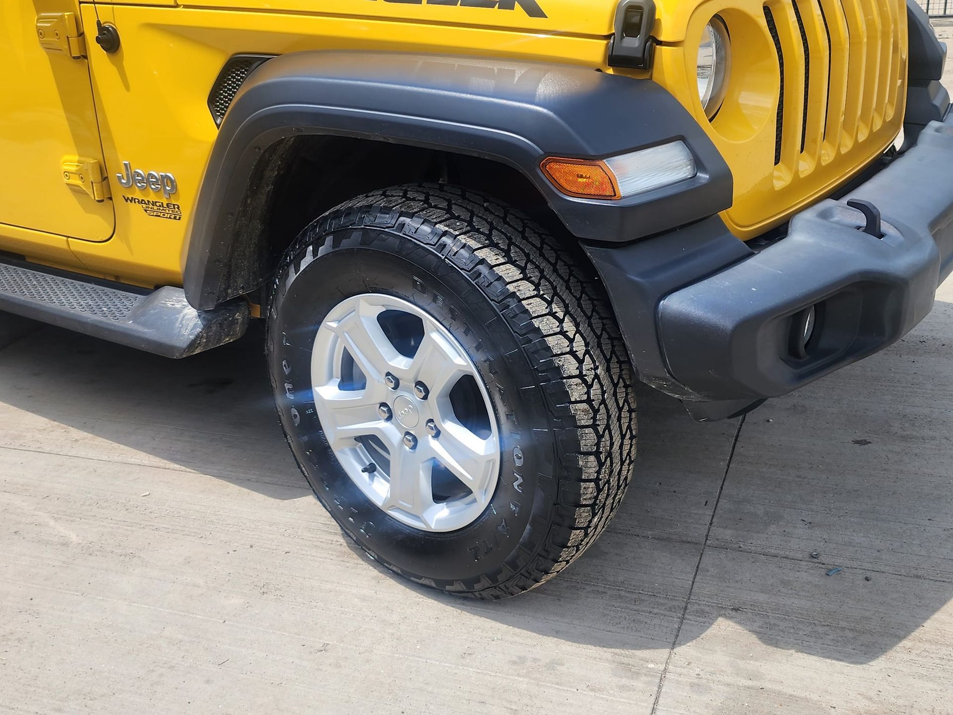 Yellow Jeep Wrangler's front wheel, showcasing tire tread and silver rim against the car's yellow body.