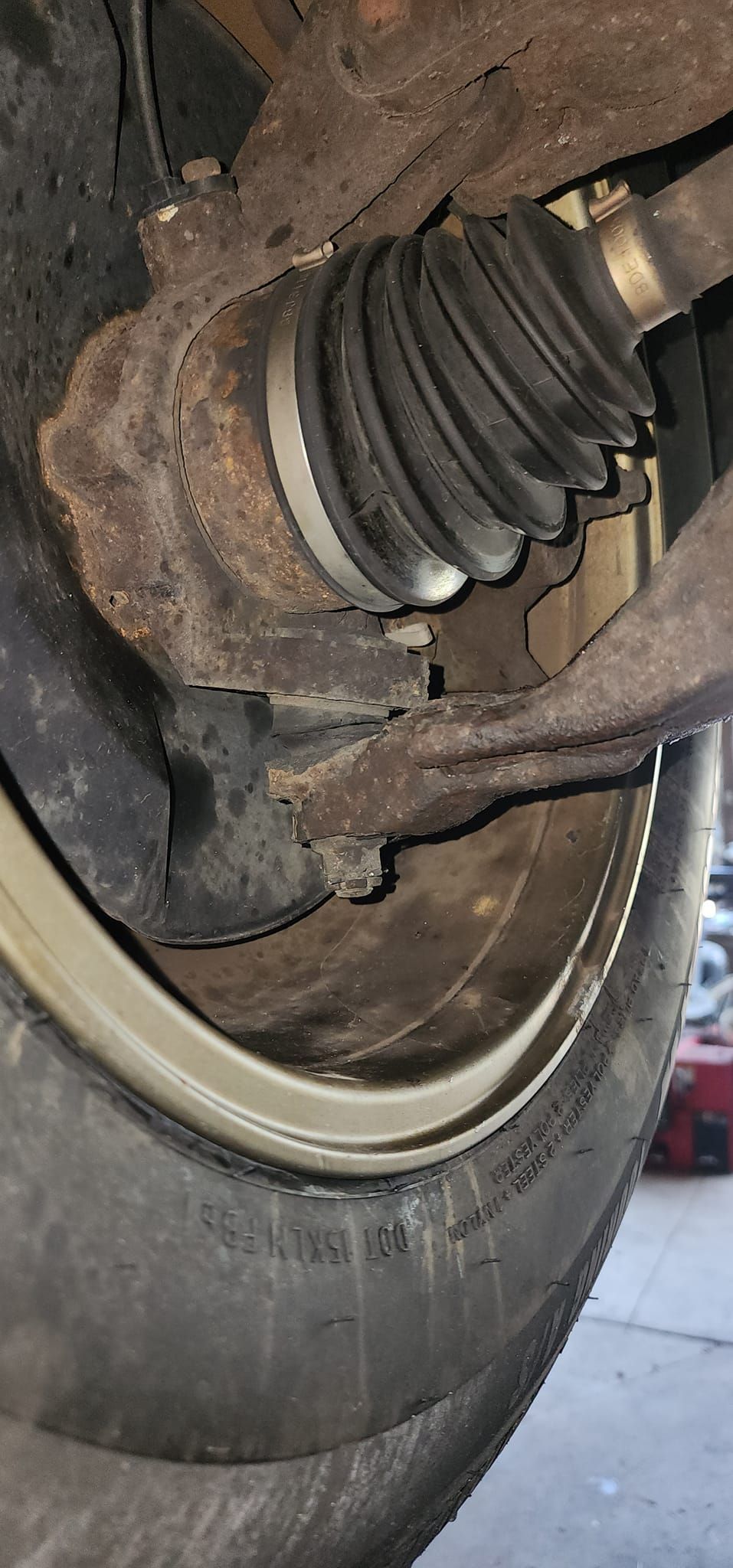 Close-up of a car's rusty suspension components: a wheel, tire, CV boot, and control arms.
