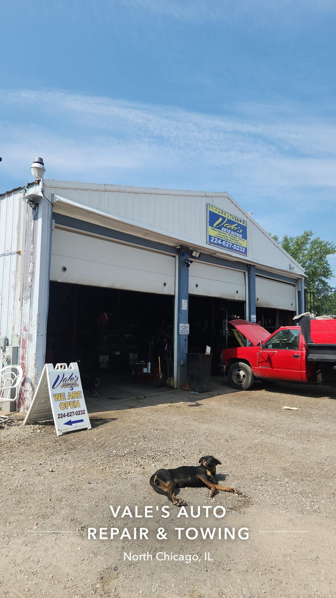 Vall's Auto Repair & Towing garage with open bay doors, red truck, dog, and a sign.