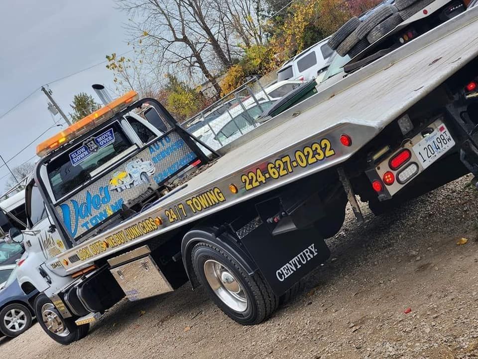 Tow truck, white, with an orange light bar, parked on gravel.