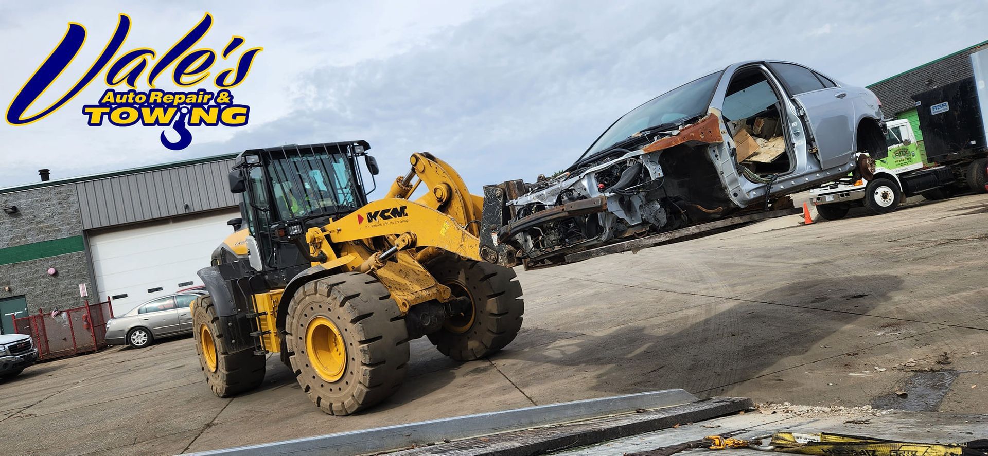 A yellow front-end loader lifts a wrecked car at Vale's Automotive Towing.