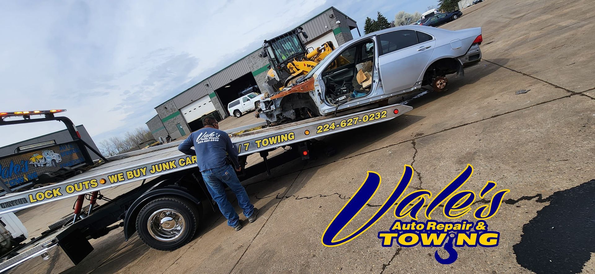 A tow truck loading a damaged silver car. A worker in blue stands on the truck. Vale's Auto Repair & Towing logo.