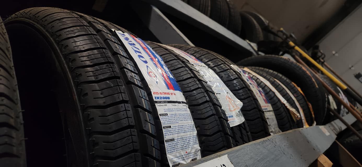 Tires stacked on a shelf in a store. The tires are black and new with price tags.