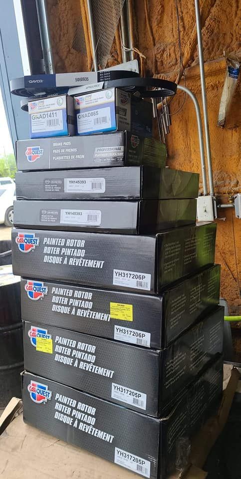 Stack of black boxes with labels and a few smaller boxes on top, likely automotive parts, in a workshop.