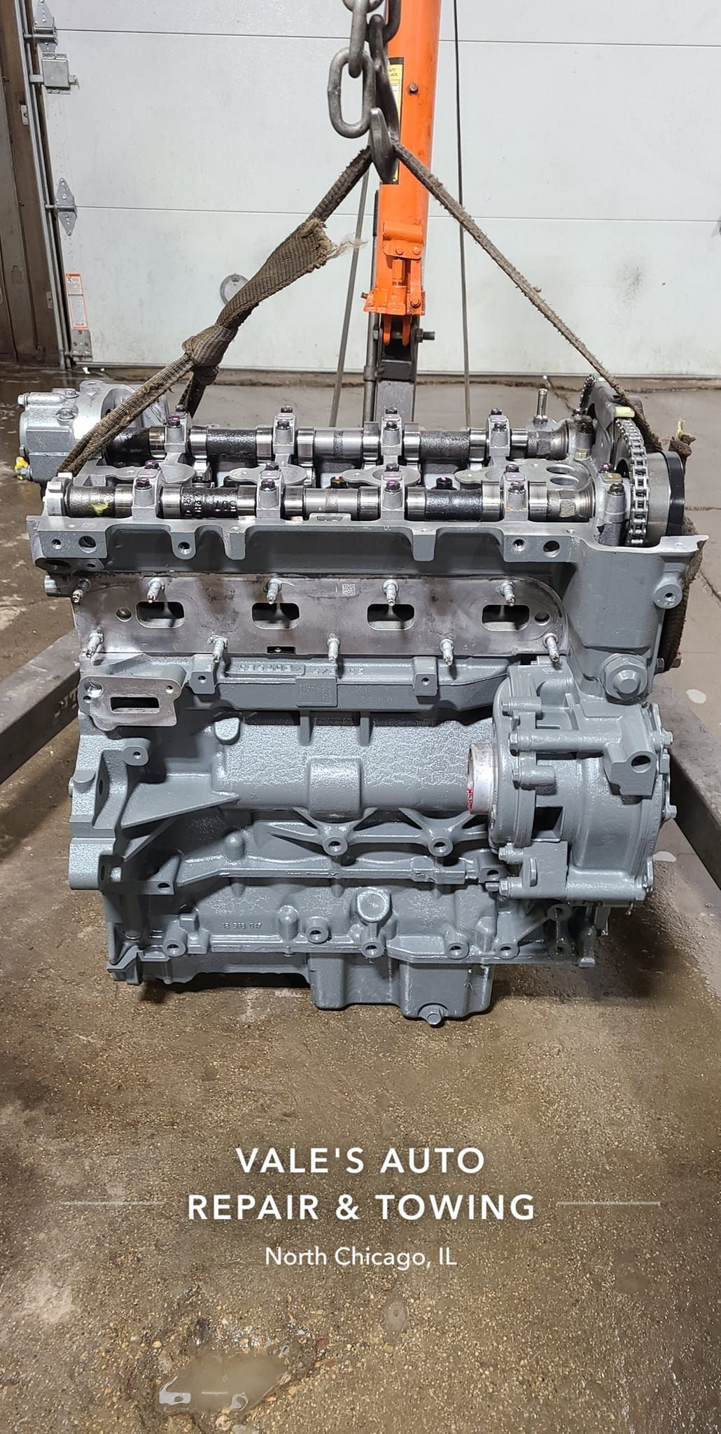 Engine suspended by a crane in a repair shop. Gray metal, orange crane, concrete floor. 