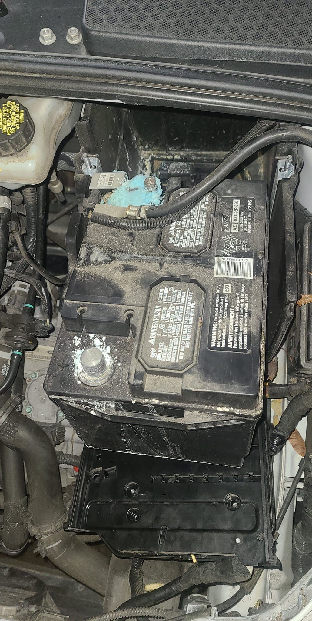 Car engine compartment with battery and fuse box covered in debris.