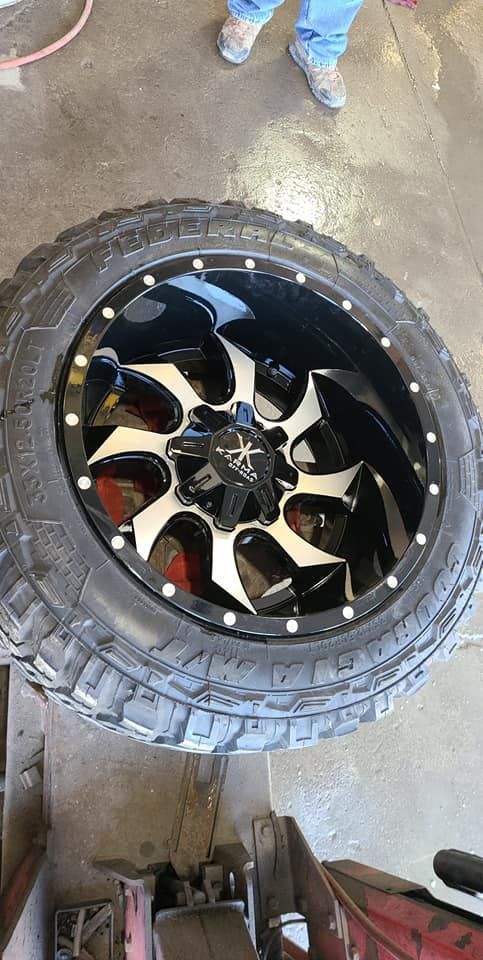 Black and silver rim and tire, person in jeans stands nearby.