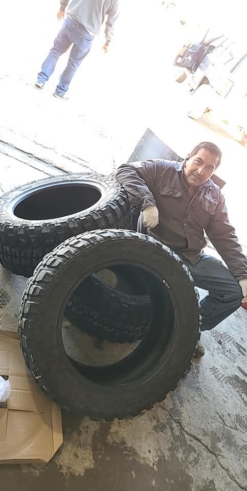 Man with tires, possibly in a garage. He is near three stacked, black tires with rugged treads.