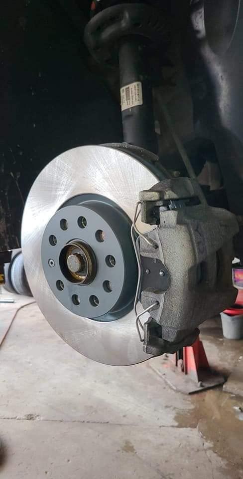 Car brake rotor and caliper assembly; silver rotor, gray caliper, red jack stand.