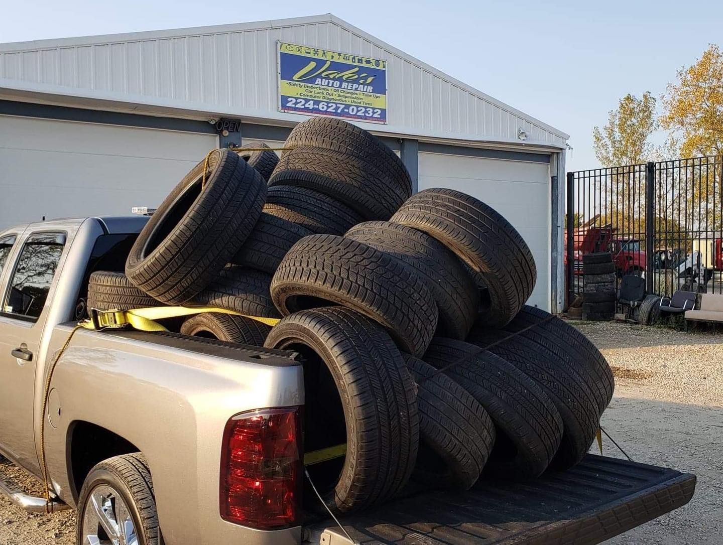 A pickup truck bed filled with a pile of used tires, in front of a blue and white building.
