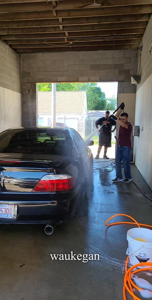 Two people washing a black car at a car wash. Water sprays from a hose.