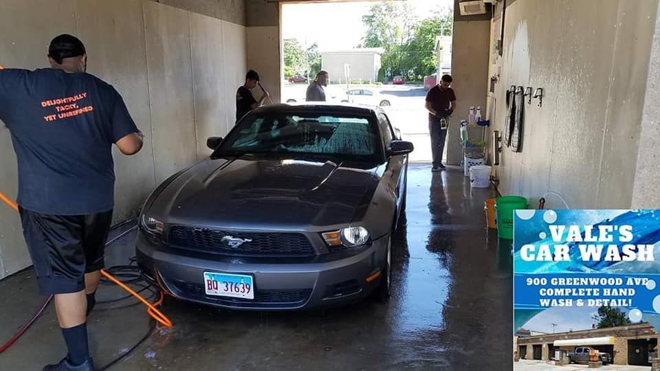 A dark gray Ford Mustang being washed at Vale's Car Wash. Two men are washing the car, another is standing in the doorway.