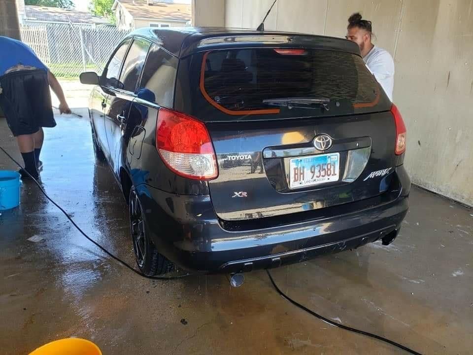 Black Toyota Matrix being washed by two people outside.