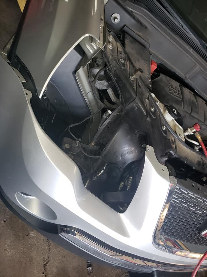 Car front end, headlight and bumper detached, showing engine components. Silver and black.