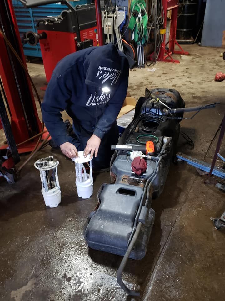Mechanic working on a car fuel tank, holding fuel pump components. Workshop setting with tools.