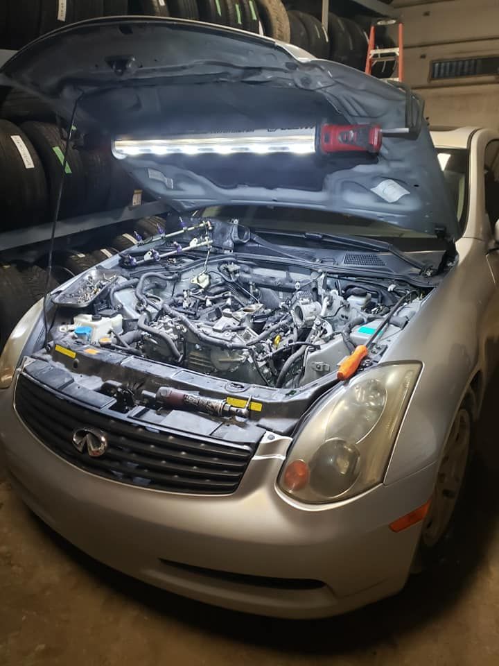 Silver car with open hood, illuminated engine bay in a garage.