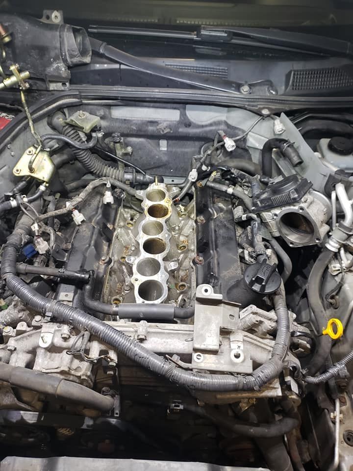 Car engine with intake manifold removed, showing exposed cylinders and various components in a workshop.