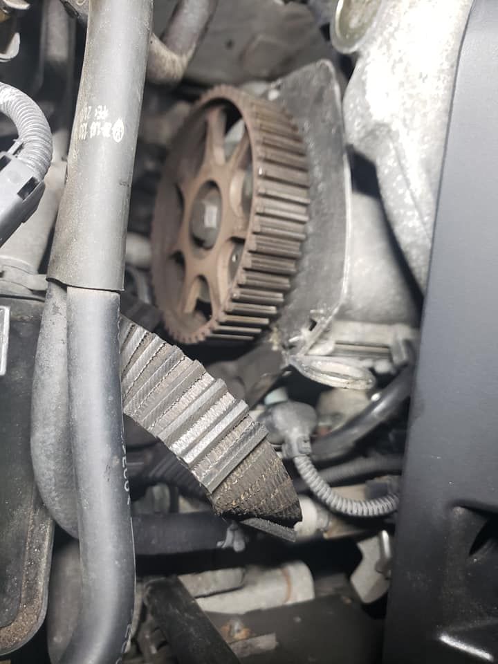 Car engine with a toothed gear, timing belt, and surrounding components.