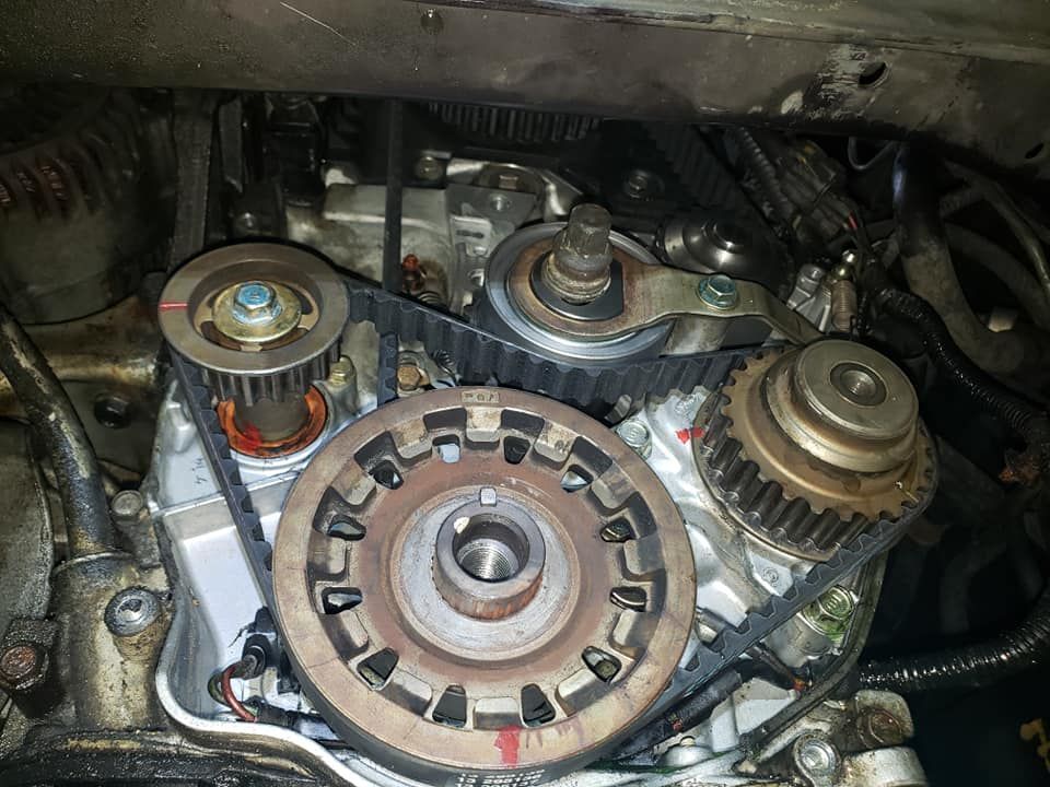 Car engine close-up showing timing belt and pulleys; red alignment marks visible.