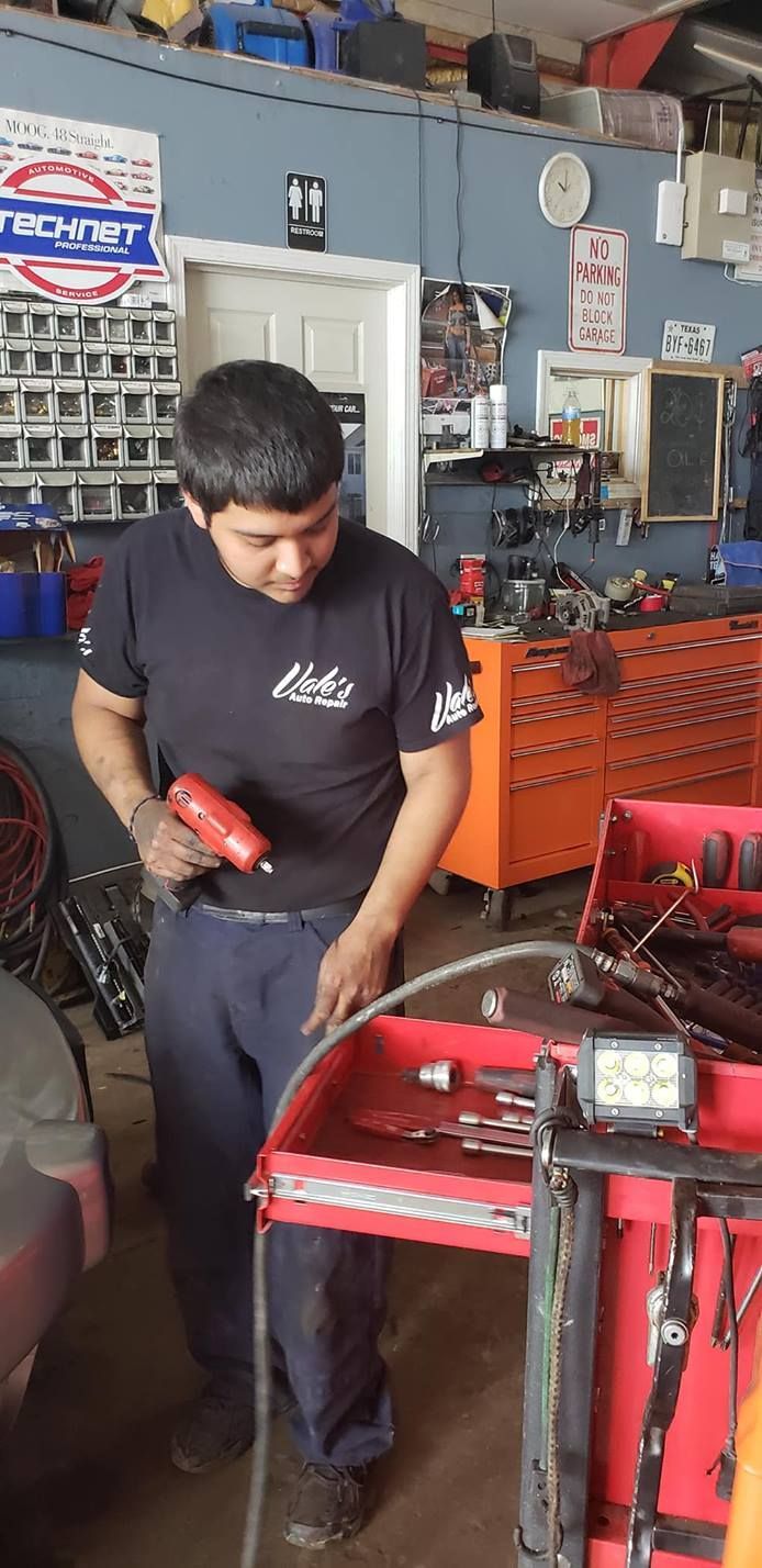 A mechanic in a garage holding a heat gun and working on a red toolbox.
