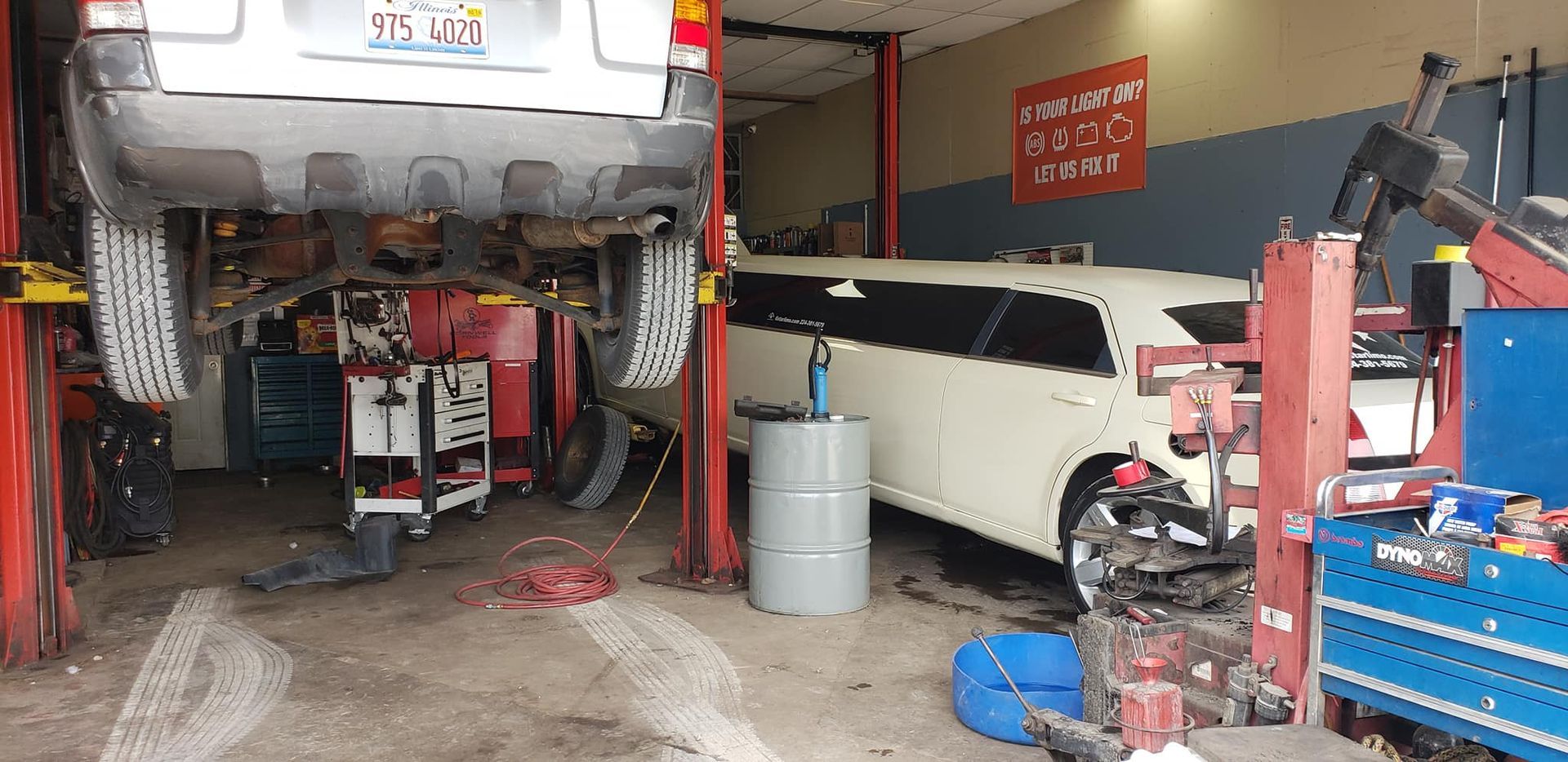 Car repair shop with car lifted on hoist and white limousine. Tools and equipment.