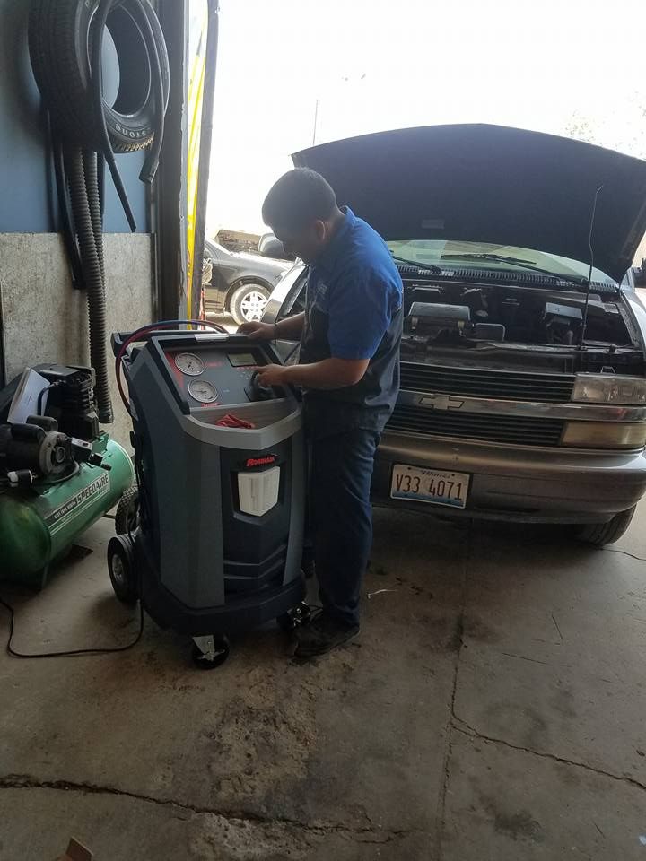 Mechanic working on car's engine with a machine in an auto shop. The car's hood is open.