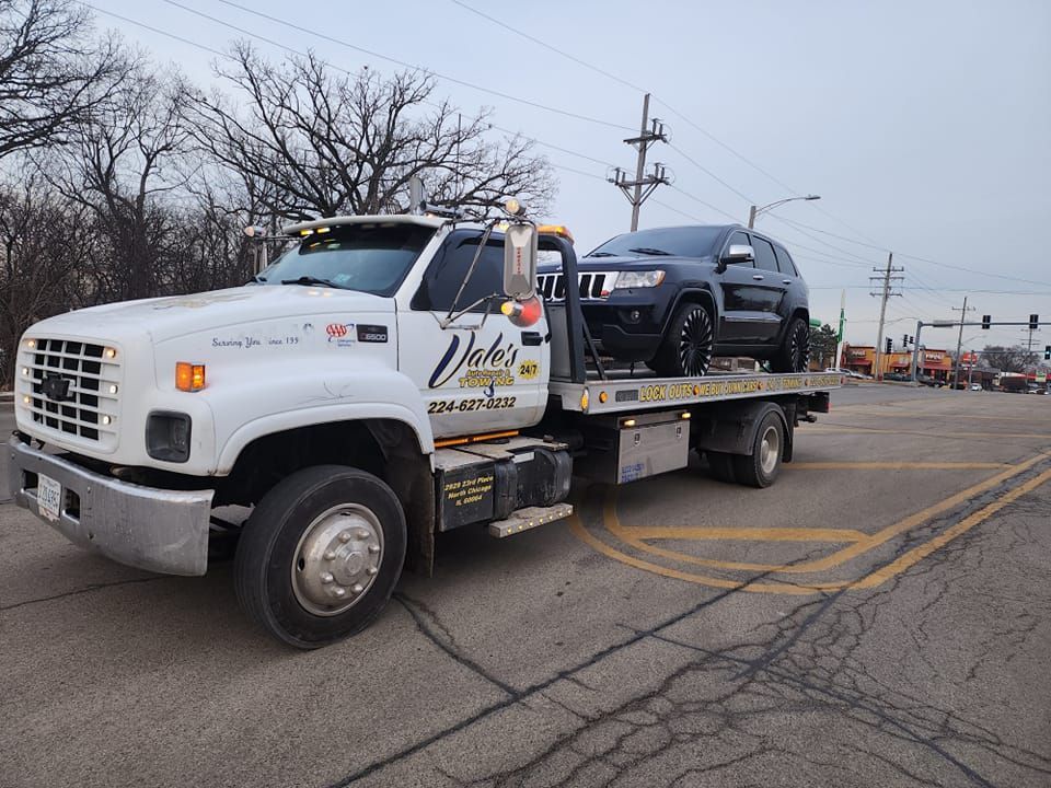 Tow truck with a black SUV on its flatbed, stopped on a road. Cloudy day.