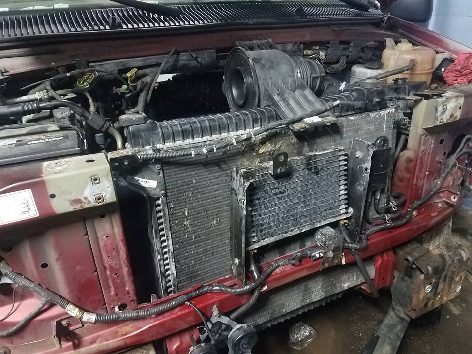 Red car engine bay with radiator, air intake, and exposed components; maintenance setting.