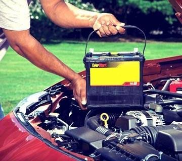 Person removing a car battery from a red car's engine bay.